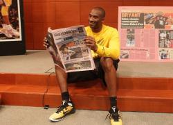 Kobe Bryant smiles as he reads an Italian newspaper.JPG